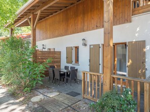 Ein überdachter Außenbereich mit Tisch und Stühlen, Holztüren und einem Holzzaun.