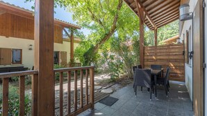 A covered patio area with a wooden pergola, outdoor seating, and a view of a building with a number '36' on the door. - 100m du Lac ! Appart avec accès Piscine (Lacanau)