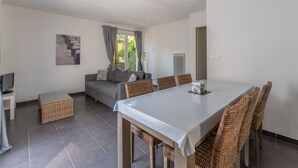 A modern living room with a dining table, sofa, and wicker chairs. - 100m du Lac ! Appart avec accès Piscine (Lacanau)