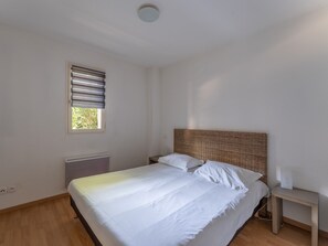 A bedroom with a bed, a nightstand, a window with blinds, a radiator, and a ceiling light.