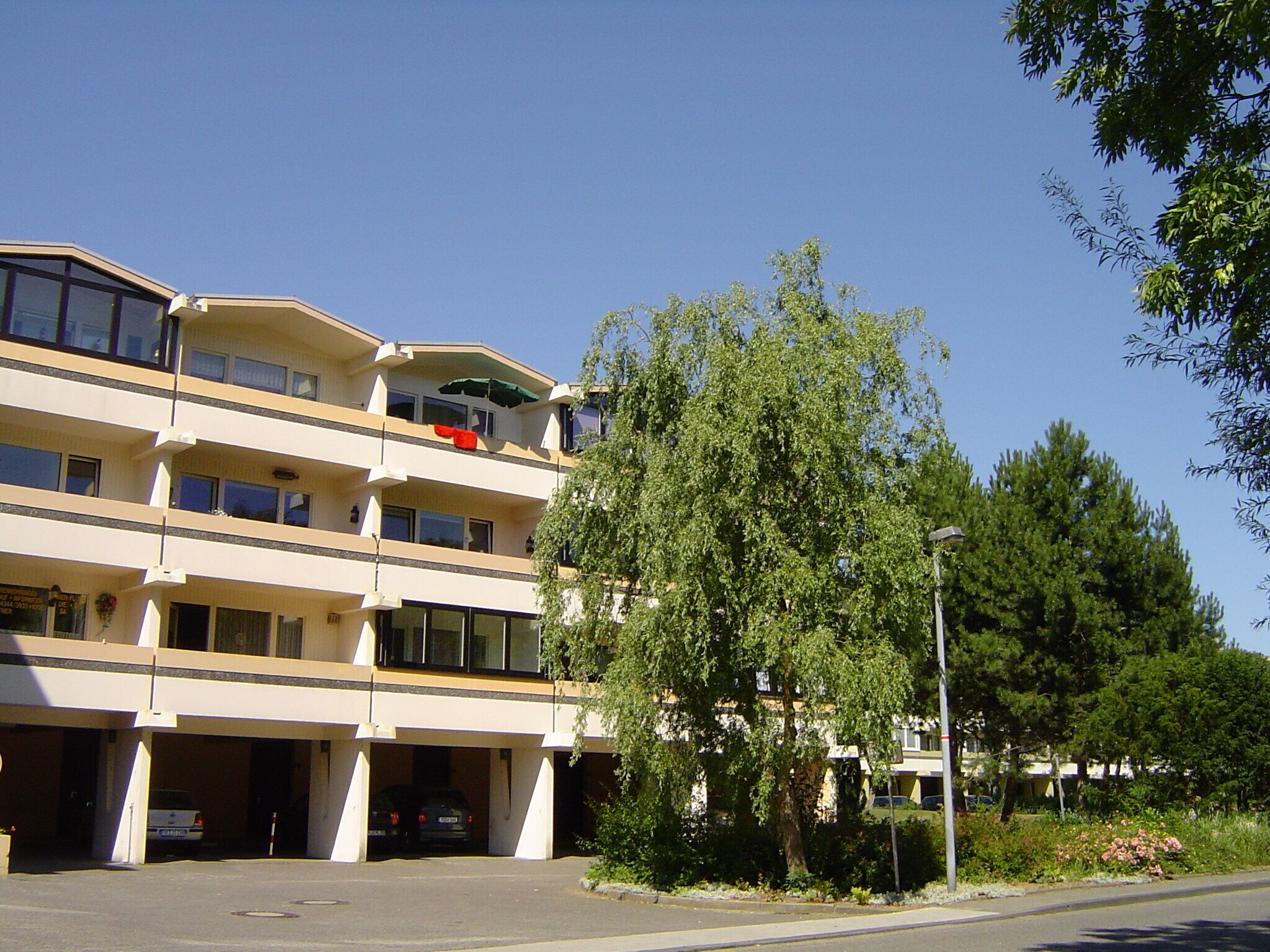A multi-story hotel with a parking garage, outdoor seating, and a large tree in front.