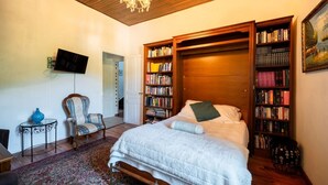 Ein Schlafzimmer mit einem Bett, einem Sessel, einem Bücherregal und einem Fernseher.