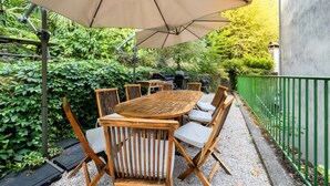 Eine Terrasse im Freien mit einem Holztisch und Stühlen, einem großen Sonnenschirm und einem grünen Zaun.