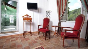 A room with a TV, two red chairs, a wooden hanger, a small table, and a view of greenery outside. - Studio "Papillon" with Mountain View, Wi-Fi, and Air Conditioning (Vals-les-Bains)