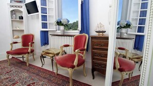 Una habitación con dos sillones tapizados de rojo, un mueble de madera, una pequeña mesa con un modelo de barco y un televisor sobre un soporte.