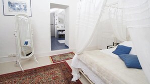 Un dormitorio con cama a dosel, un espejo, un tapete rojo estampado y un pasillo que conduce a un baño.