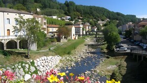 Un pueblo junto al río con muros de piedra, un puente y coches estacionados.