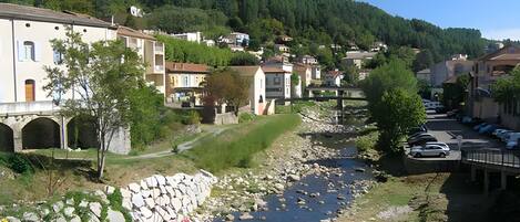 Un pueblo junto al río con muros de piedra, un puente y coches estacionados.
