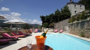 A poolside area with lounge chairs, a table with a champagne bottle and glasses, and a stone wall.