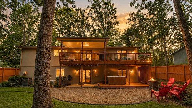Une maison à deux étages avec un balcon, un jacuzzi et un foyer extérieur dans le jardin.