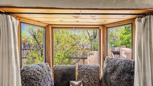 A cozy seating area with a view of trees and a wooden deck. - Historic Adobe, Kiva Fireplace, Walk to Canyon Rd (Santa Fe)
