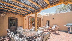 An outdoor patio with a covered seating area, a grill, and a table with chairs. - Historic Adobe, Kiva Fireplace, Walk to Canyon Rd (Santa Fe)