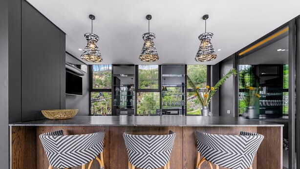 A modern kitchen with a bar area, three hanging pendant lights, and a large window offering a view of greenery. - Tarentaal Kloof Villa in Higgovale. (Cape Town)