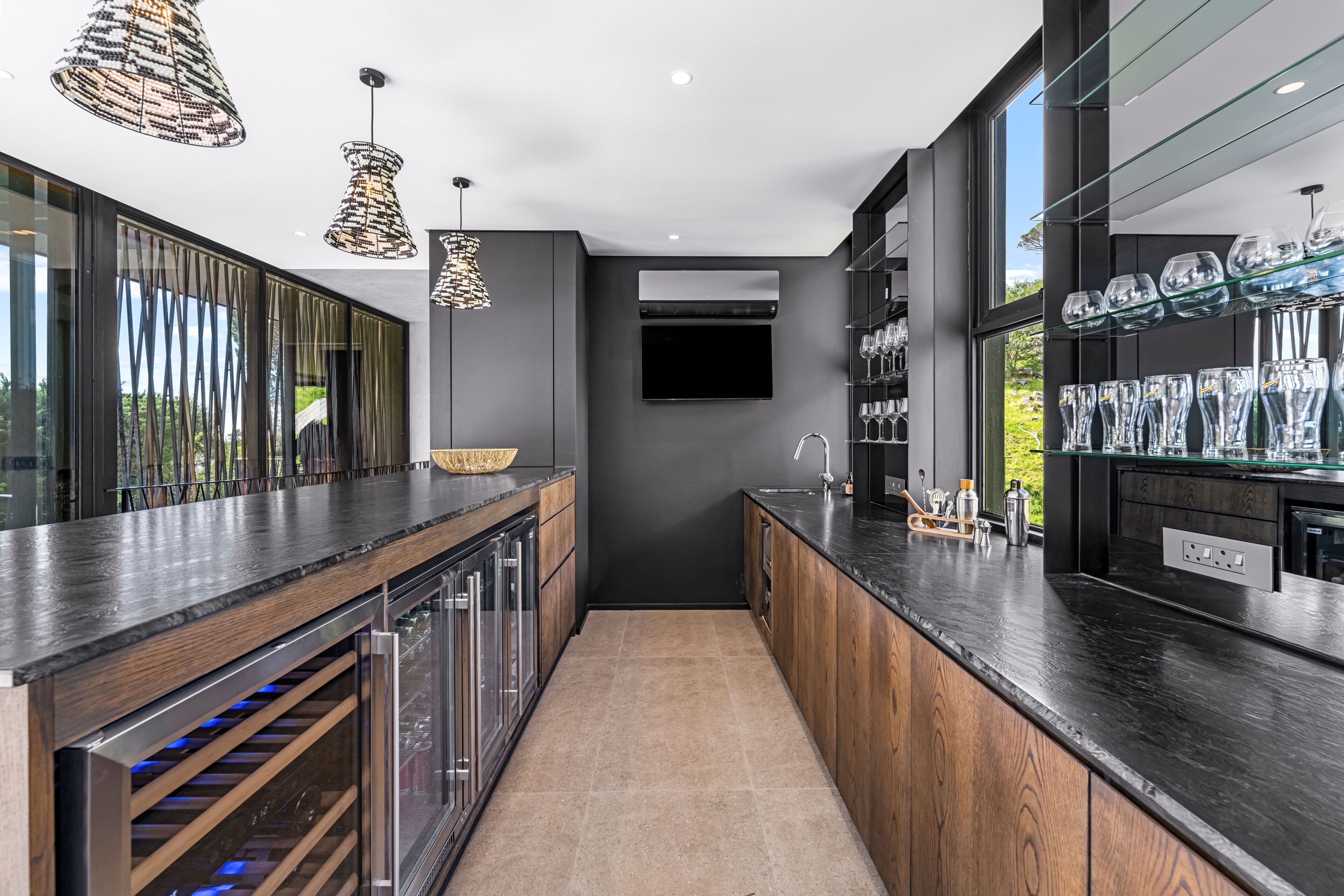 Une cuisine moderne dotée d’un meuble à bouteilles, d’une cave à vin intégrée et de luminaires suspendus.
