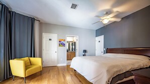 Ein Schlafzimmer mit einem Bett, einem gelben Sessel, Holzboden, einem Deckenventilator und einer Tür zu einem Badezimmer.