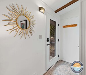 A white door with a glass panel, a gold sunburst mirror, a wooden coat rack, and a logo for 'Vacation Rental Property Partners'. - Pet-Friendly Lake Como Retreat, Private Backyard, Boat Parking (Lake Geneva)