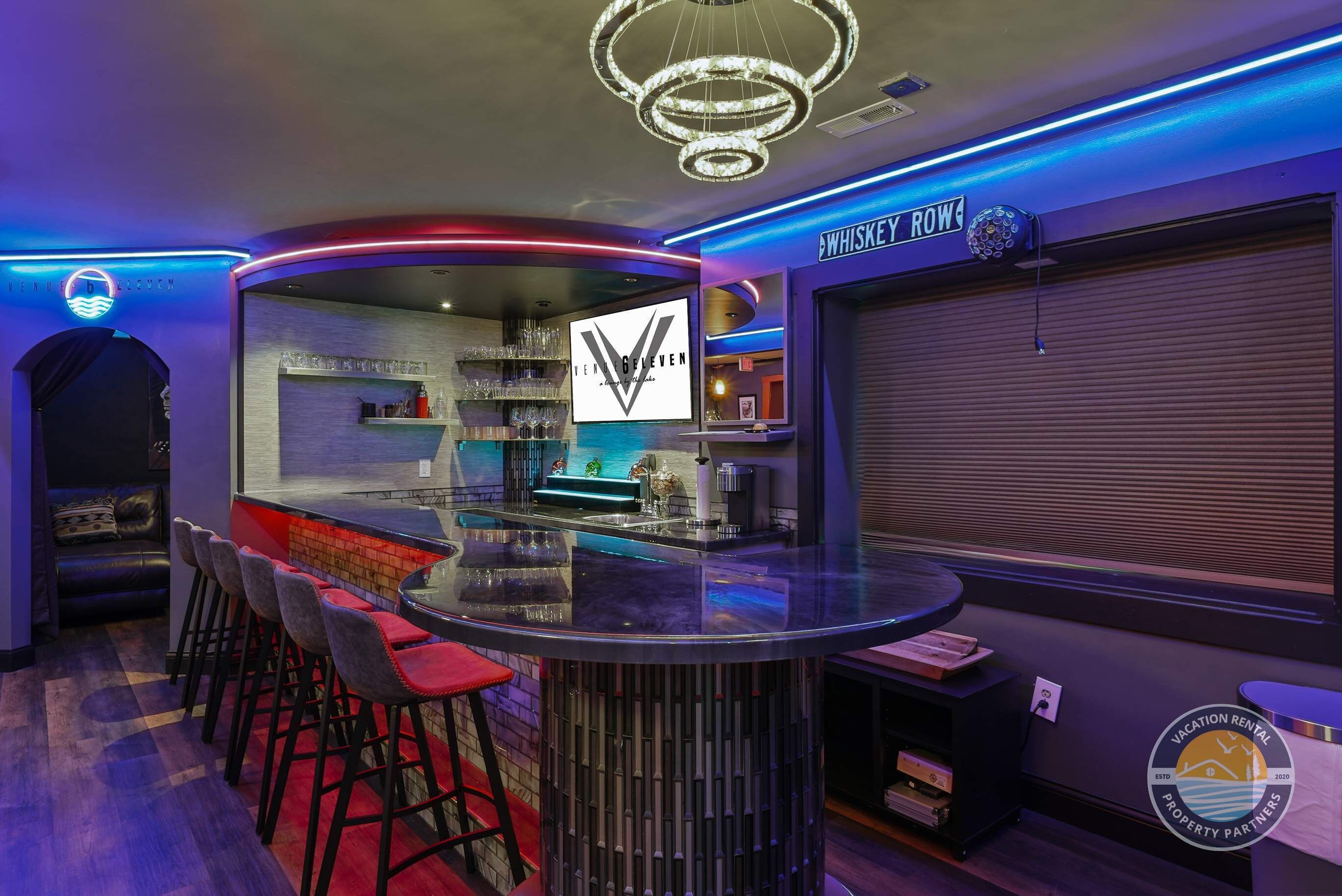 A bar area with stools, a counter, and a neon sign.