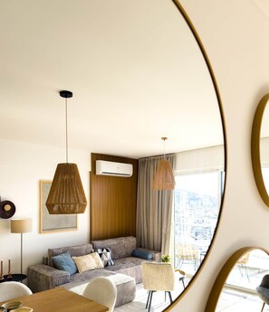 A modern living room with a sofa, a dining table, and a view of the city through large windows. - Turul - Panoramic View (Saranda)