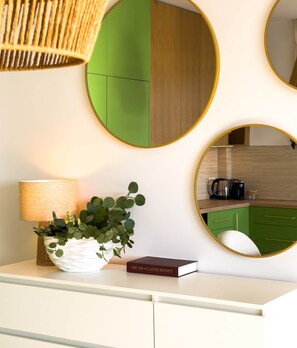 A modern kitchen with green cabinets, a round mirror, a potted plant, a book, and a lamp on a white countertop. - Turul - Panoramic View (Saranda)