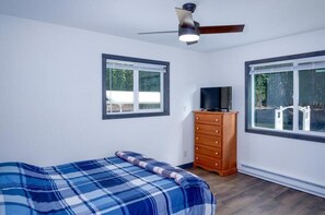 Un dormitorio con cama, cómoda, ventilador de techo y dos ventanas.