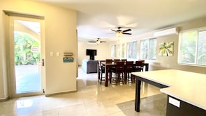 A spacious living area with a dining table, chairs, a ceiling fan, a flat-screen TV, and a sign on the wall. - Spacious 5BR 4.5BA Home Private Pool Walk to Beach (Rincon)