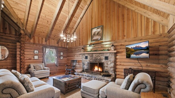 A log cabin interior with a stone fireplace, wooden walls, and a mounted television. - Townsend Charm: River View Historic Log Cabin! (Townsend)