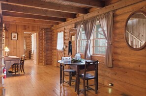A wooden cabin interior with a dining table, chairs, a small house model, and a fire extinguisher. - Townsend Charm: River View Historic Log Cabin! (Townsend)