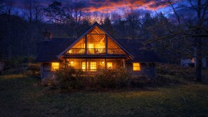 A log cabin with a balcony, surrounded by trees and a grassy area. - Townsend Charm: River View Historic Log Cabin! (Townsend)