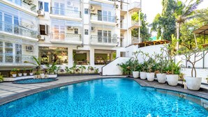 A swimming pool with a tiled floor, surrounded by potted plants and a multi-story building with balconies. - Staymaster Solintra 2BHK C401 (Verem)