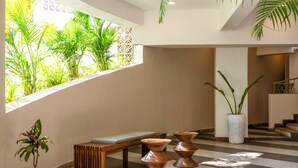 A modern interior with a bench, two copper planters, and a large window overlooking greenery. - Staymaster Solintra 2BHK C401 (Verem)