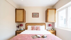 A hotel room with a bed, two nightstands, a window, and a wall-mounted artwork. - Staymaster Solintra 2BHK C401 (Verem)