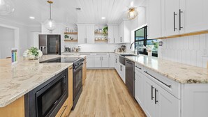 Een moderne keuken met witte kasten, een marmeren aanrecht en roestvrijstalen apparatuur.