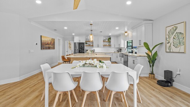 Een moderne keuken met witte kasten, een centraal eiland en een eetgedeelte met witte stoelen.