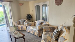 A spacious living area with a sofa set, a fan, and a decorative wall plaque. - Beautiful 3-Bedroom Home with Pool in Signal Hill (Signal Hill)