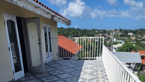 A tiled balcony with a railing, a door, and a view of a residential area in the background. - Beautiful 3-Bedroom Home with Pool in Signal Hill (Signal Hill)