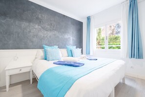 Une chambre à coucher avec un lit, une table de chevet blanche, un mur d’accent de couleur grise et une fenêtre avec des rideaux.