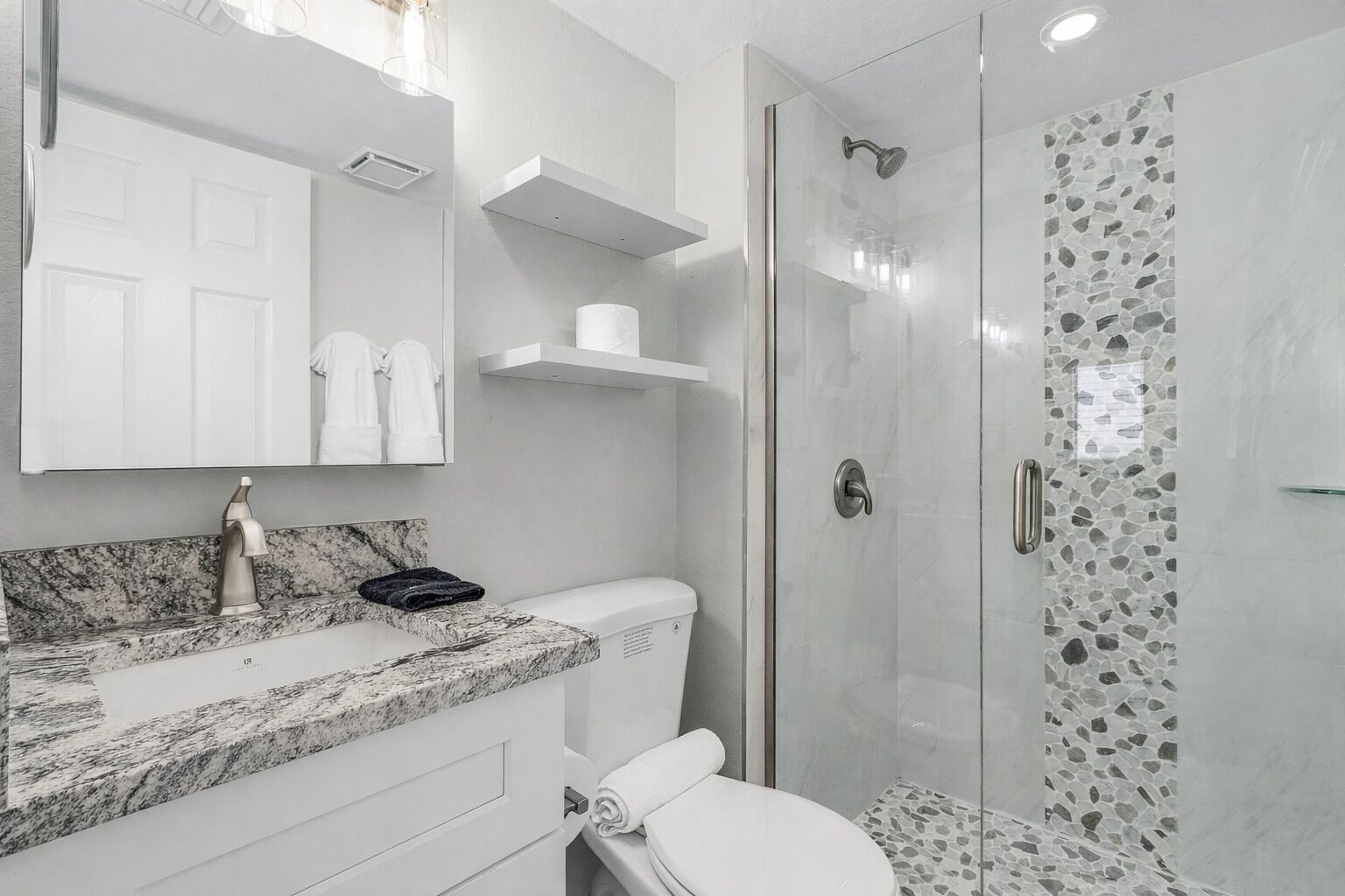 A modern bathroom with a marble countertop, a toilet, a glass shower enclosure, and a mirror with a door.