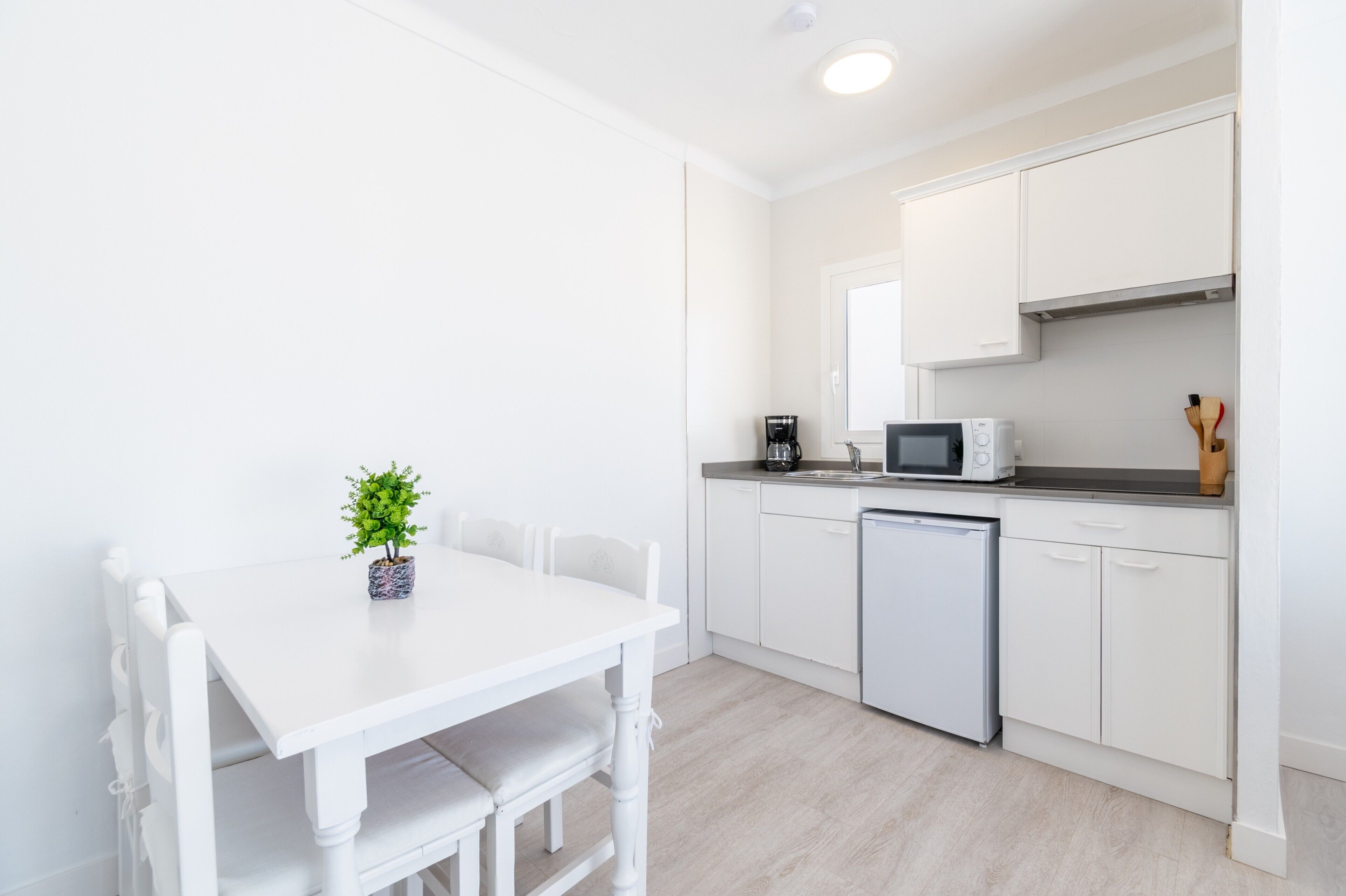 Una cocina moderna con armarios blancos, una mesa de comedor blanca y una pequeña planta en maceta.