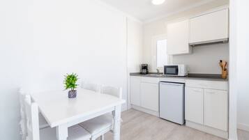 Una cocina moderna con armarios blancos, una mesa de comedor blanca y una pequeña planta en maceta.
