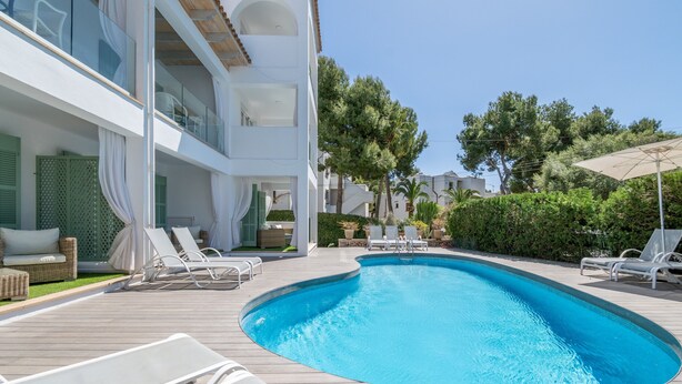 A swimming pool with lounge chairs, a wooden deck, and a building with balconies. - 1-Bedroom Apartment 'G' with Sofa Bed, Shared Pool, Wi-Fi & Air Conditioning (Felanitx)