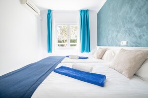 Habitación de hotel con cama, ventana con cortinas, aire acondicionado y pared con textura.
