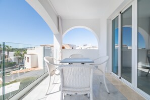 Un balcón con una mesa, sillas, un ventanal de vidrio y vista a edificios.