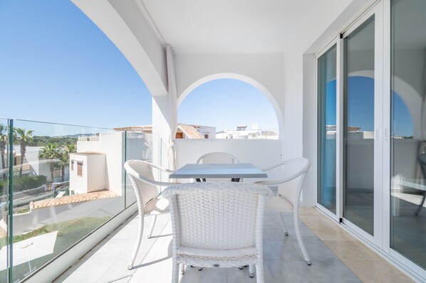 A balcony with a table and chairs, a glass door, and a view of buildings. - 2-Bedroom Apartment 'F' with Shared Pool, Wi-Fi, and Air Conditioning (Felanitx)