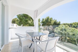 A balcony with a table and chairs, a glass railing, and a view of trees and buildings. - 2-Bedroom Apartment 'F' with Shared Pool, Wi-Fi, and Air Conditioning (Felanitx)