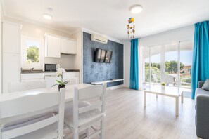Una sala moderna con comedor, televisor montado en la pared y un balcón con cortinas azules.