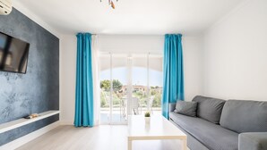 A modern living room with a grey sofa, a white coffee table, and a TV mounted on a grey wall. - 2-Bedroom Apartment 'F' with Shared Pool, Wi-Fi, and Air Conditioning (Felanitx)