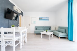 Een moderne woonkamer met een flatscreen-tv, een bank, een eettafel met stoelen en een klein bijzettafeltje.