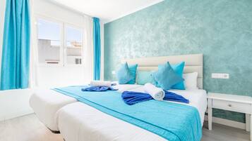 A hotel room with a bed, a nightstand, a window with curtains, and a teal-colored wall.