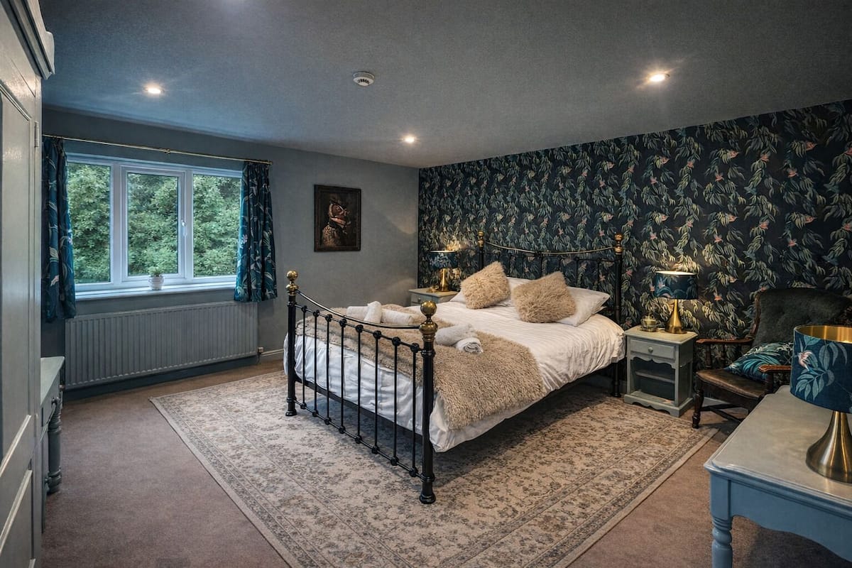 A bedroom with a bed, a nightstand, a chair, a window, and a radiator.
