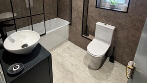 Une salle de bain moderne avec une baignoire, des toilettes et un grand lavabo posé sur un plan de travail noir.